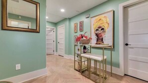 Un pasillo con paredes verde azulado, piso de madera, un banco, un espejo y una puerta.