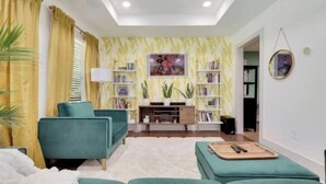 Una sala de estar con sofás color turquesa, un mueble de entretenimiento blanco y un papel tapiz amarillo estampado.