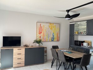 Eine moderne Küche mit Essbereich, inklusive Flachbildfernseher, Deckenventilator und einem farbenfrohen, abstrakten Gemälde.