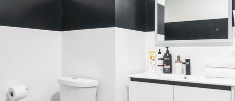 Une salle de bain moderne avec des toilettes blanches, des murs rayés de noir et de blanc, un lavabo blanc avec un miroir et des carreaux hexagonaux noirs sur le sol.