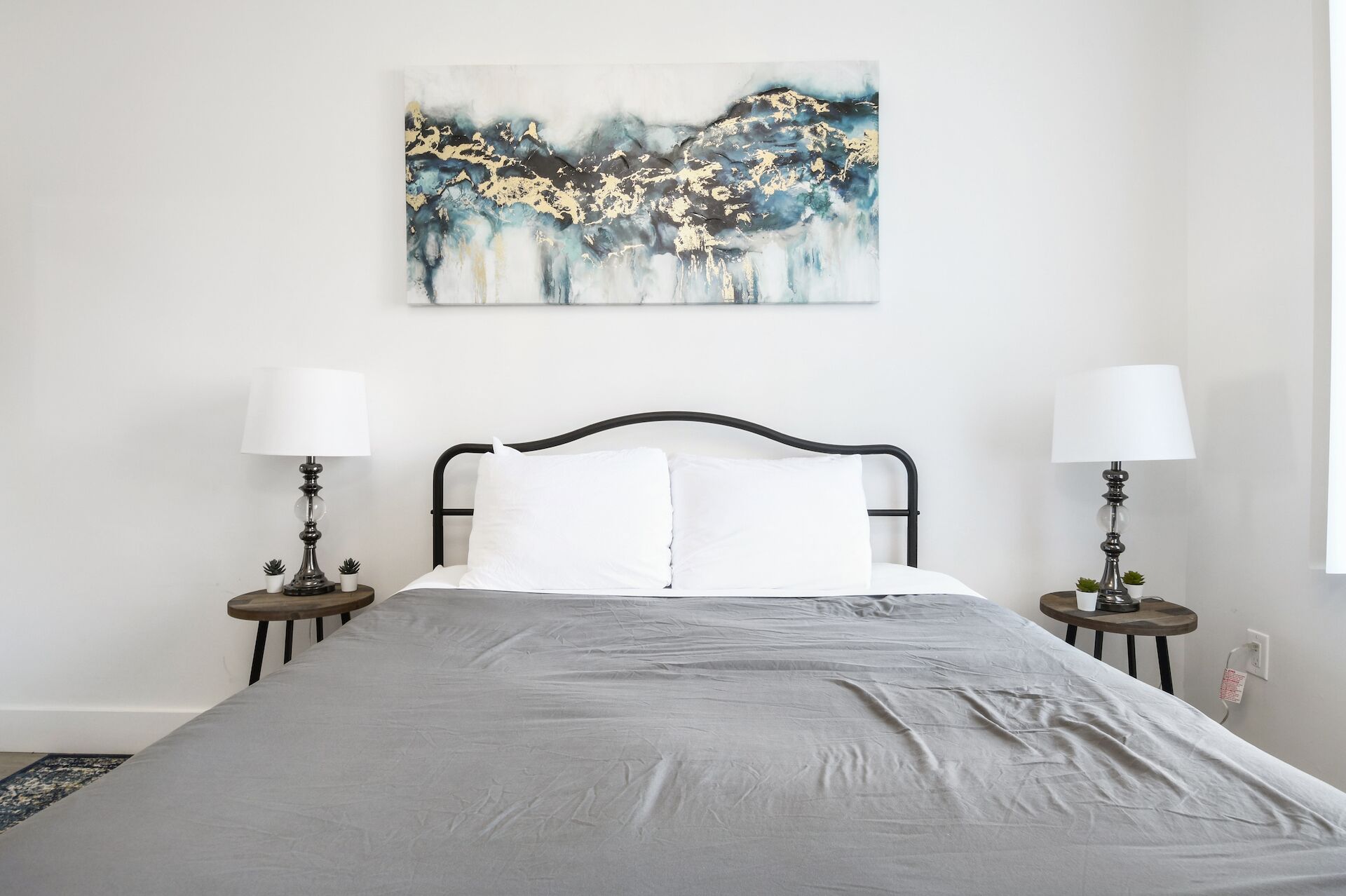 A neatly made bed with white linens, two bedside lamps, and a modern abstract painting on the wall.