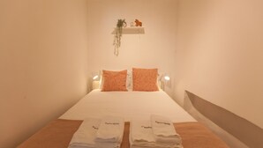 A neatly made bed with two pillows, a small shelf with a plant and a figurine, and two folded towels on the bed.