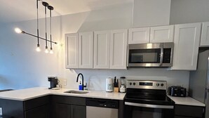 Une cuisine moderne avec des meubles blancs, un four à micro-ondes en acier inoxydable, une cuisinière noire et un lave-vaisselle.