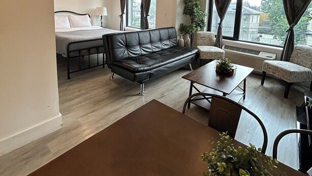 Un salon moderne avec un canapé en cuir noir, une table à manger en bois avec des chaises, une petite table basse et une grande fenêtre avec des rideaux.