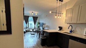 Une cuisine moderne dotée d’un îlot central, d’un coin repas avec une table et des chaises, et offrant une vue sur une maison par le biais d’une fenêtre.
