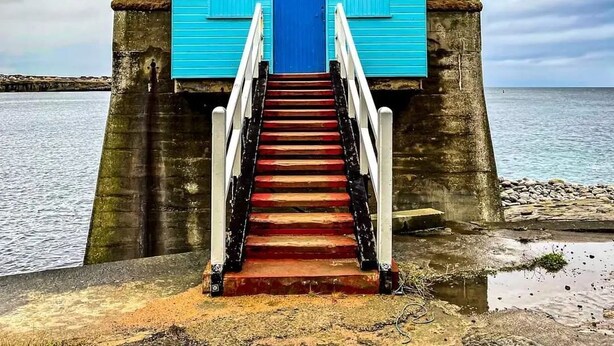A coastal building with a blue door and a staircase leading up to it. - Apartment 65B (Thurso)