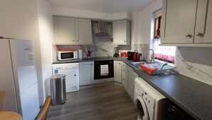 A compact kitchen with a microwave, oven, sink, and washing machine. - Apartment 65B (Thurso)