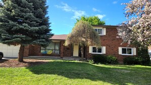 Una casa a due piani in mattoni con un cortile anteriore, un garage e un albero.