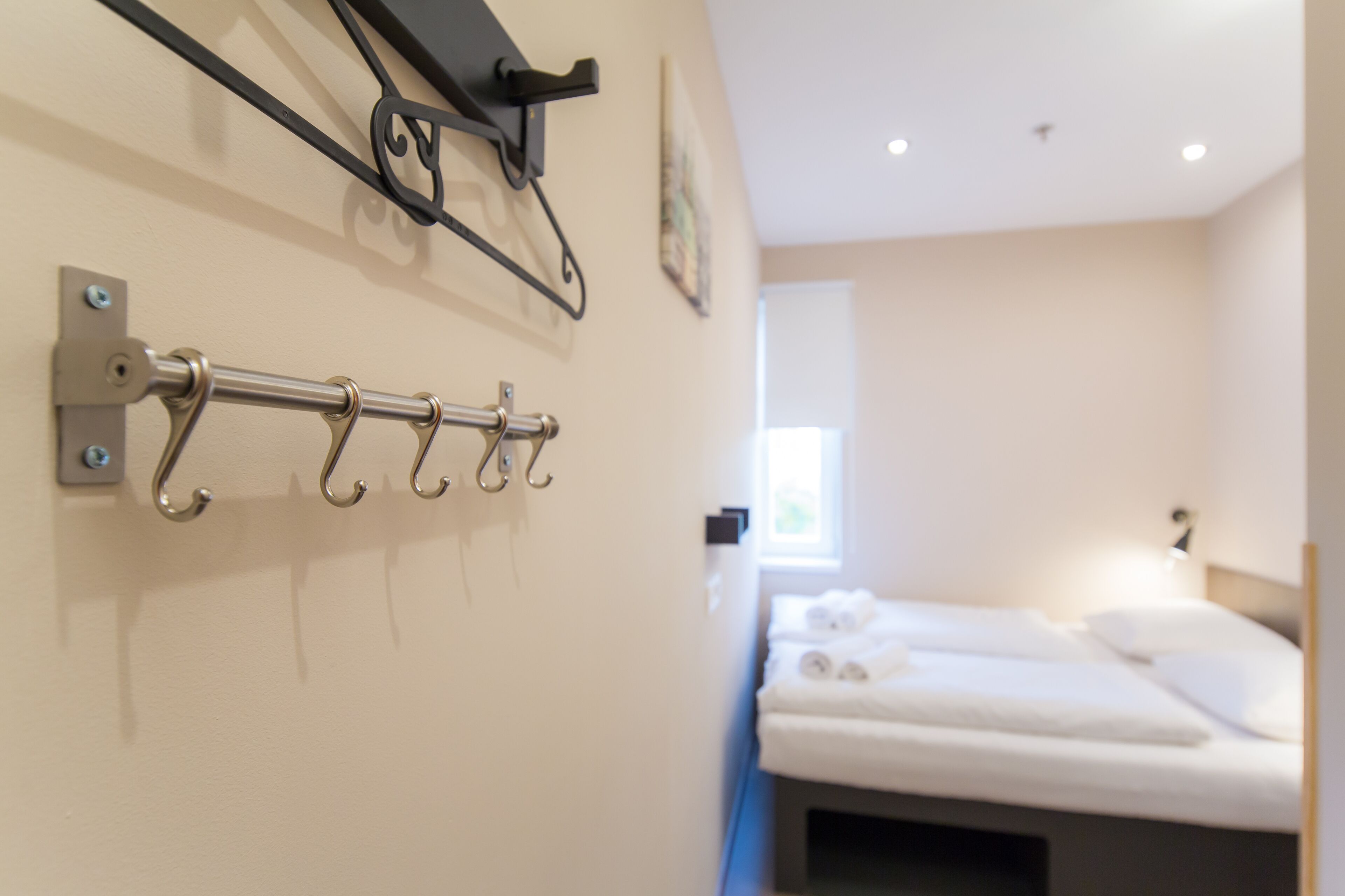 Una habitación de hotel con una cama, un perchero en la pared y una ventana.