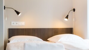 A neatly made bed with white linens, two bedside lamps, and a power outlet on the wall. - Minimino hotel (Prague)