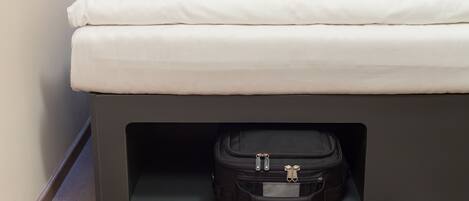 A neatly made bed with white linens and a black suitcase placed under a bed frame.