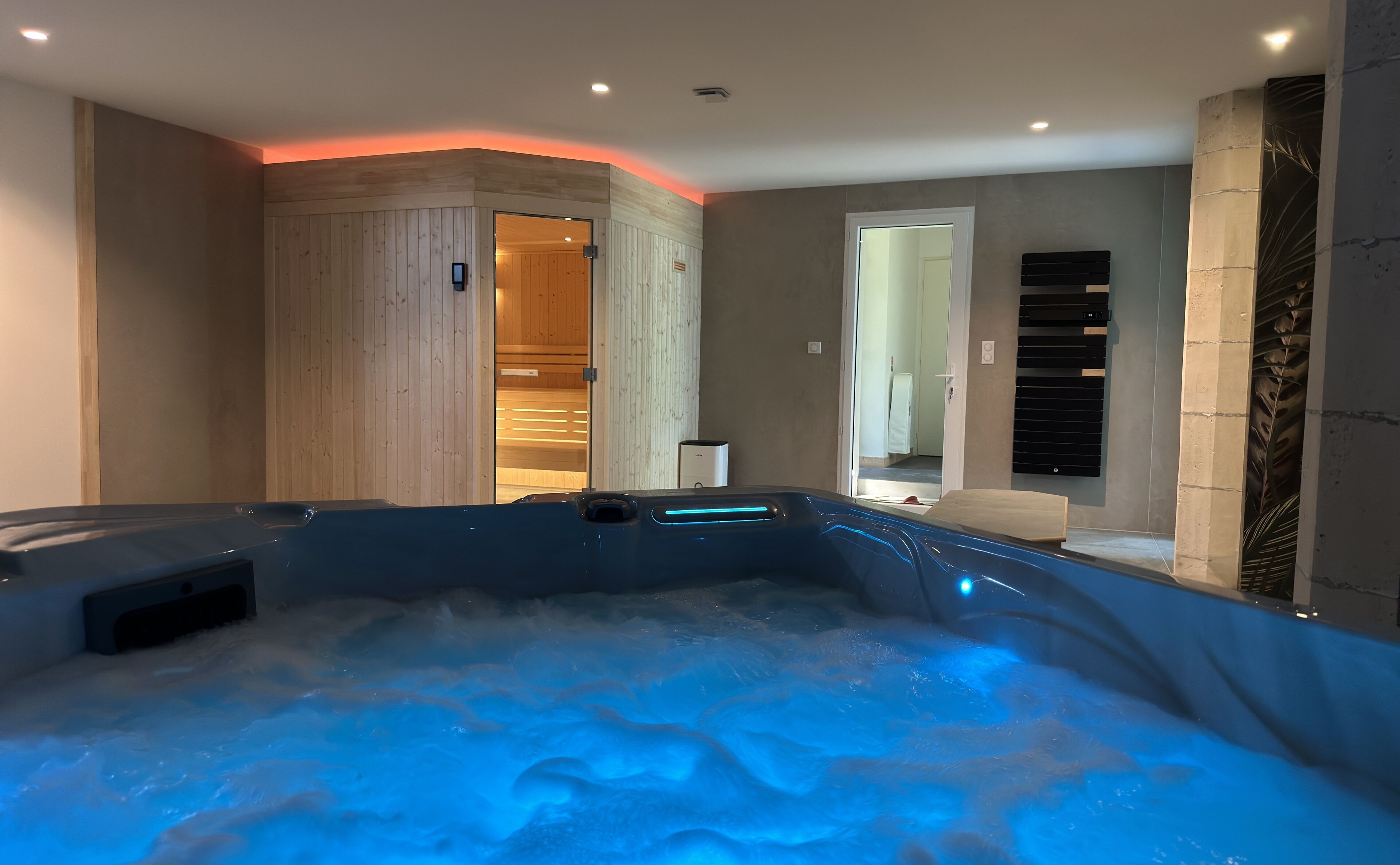 Moderni spa-huone, jossa on poreallas, puupaneloidut seinät ja tyylikäs musta lämmitin.