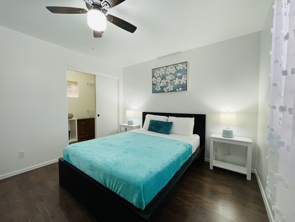 A bedroom with a bed, two bedside tables with lamps, a ceiling fan, a door, and a painting on the wall. - Gorgeous Sanctuary: A Cozy 3- Bedrooms Hide-out in Mesa (Mesa)