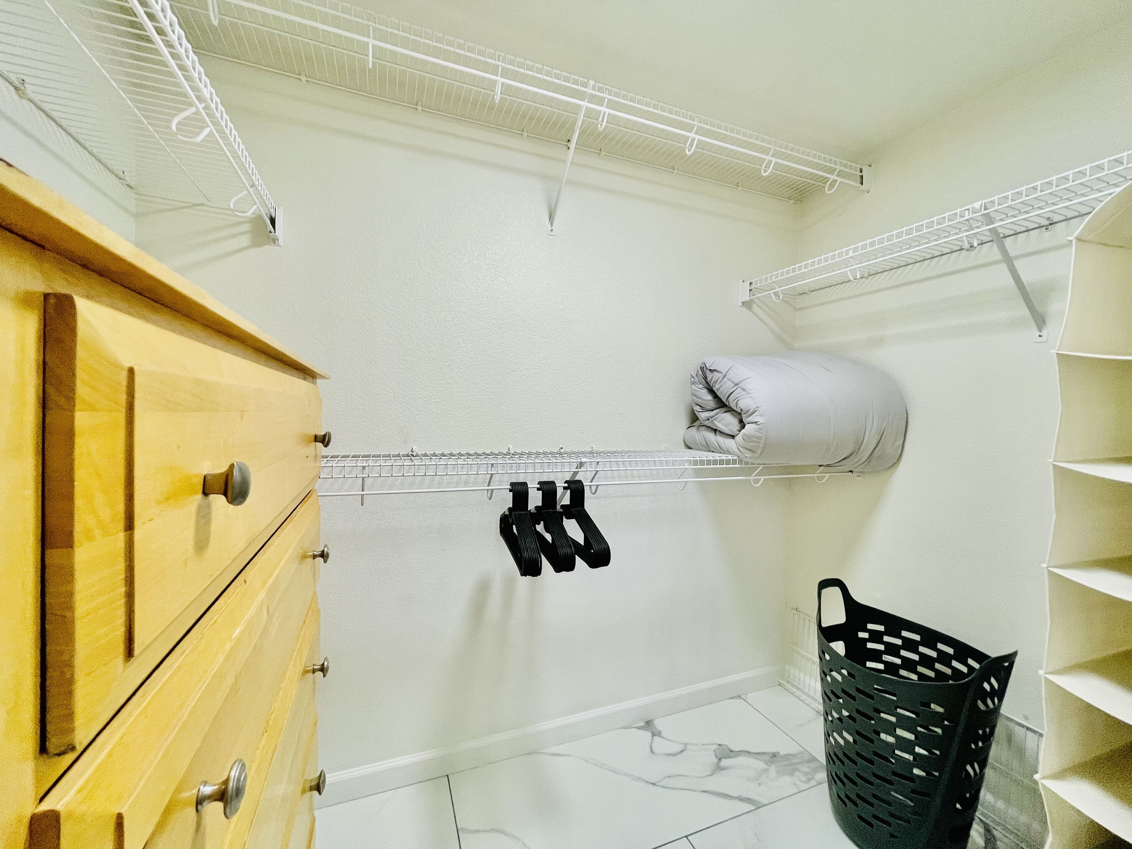 Ein Waschbereich mit einem Wäscheständer aus Metall, einem Holzschrank, einem schwarzen Wäschekorb und einem aufgerollten Handtuch.