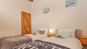 A bedroom with two beds, a wooden door, a radiator, and a wall with two paintings. - Adelaide's Cottage (Pickering)