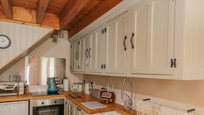 A kitchen with white cabinets, a wooden countertop, a sink, a toaster, and a clock on the wall. - Adelaide's Cottage (Pickering)