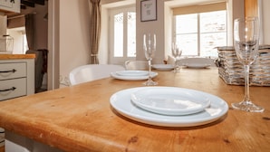 A dining table set with plates and wine glasses, wooden beams on the ceiling, and a window with curtains. - Adelaide's Cottage (Pickering)