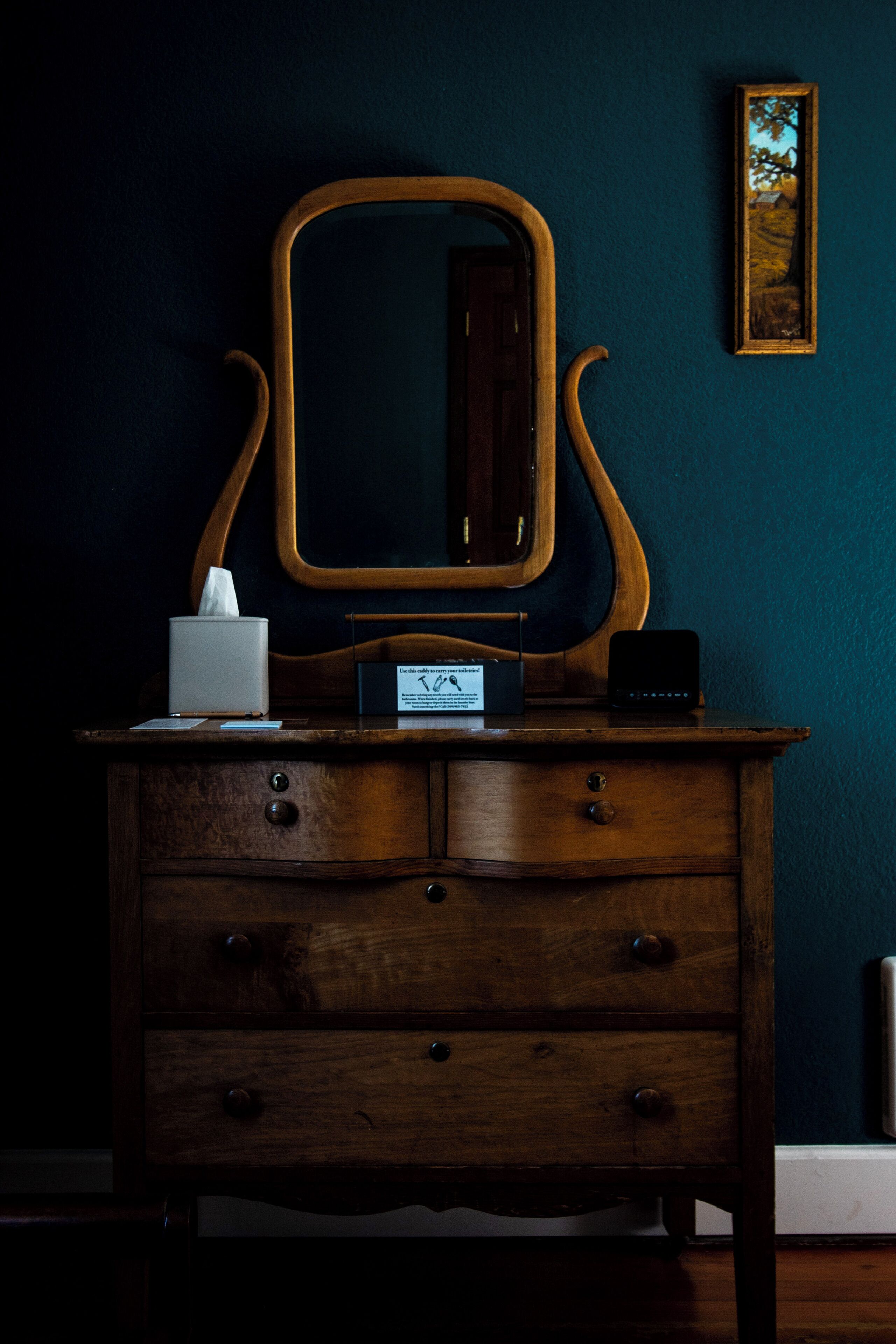Un comò in legno con specchio, un portatovaglioli e un piccolo dispositivo elettronico.