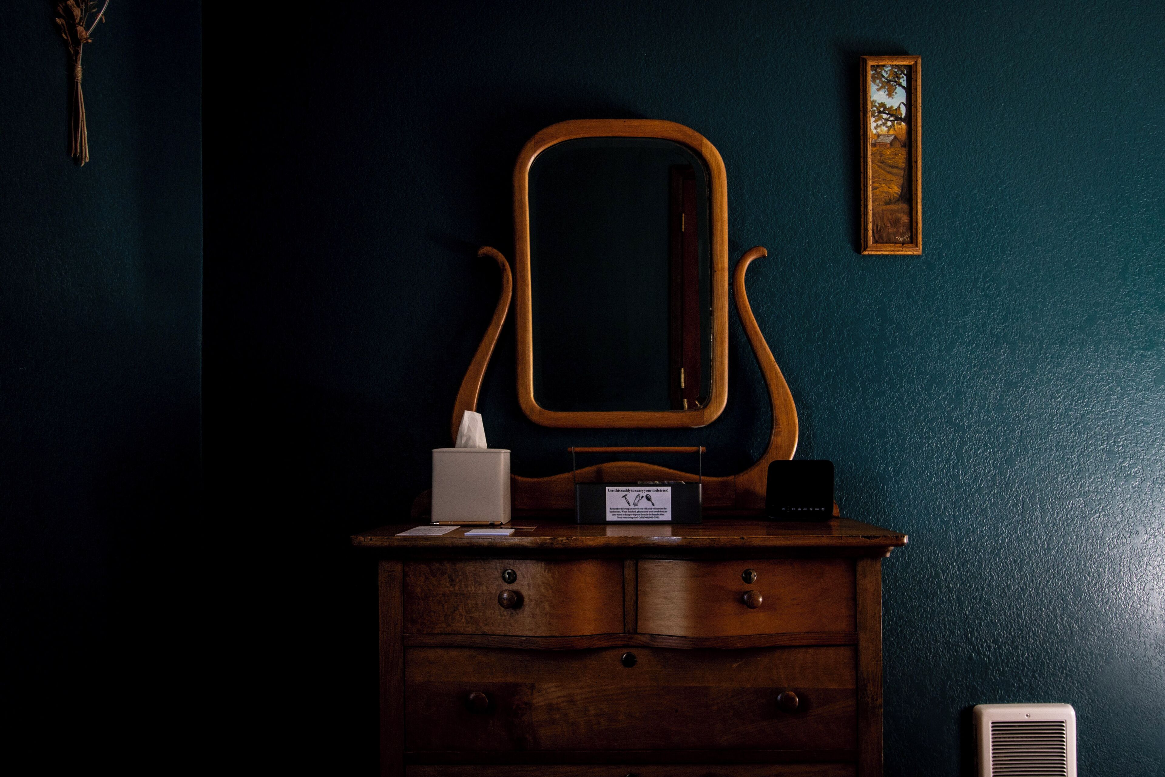 A wooden dresser with a mirror, a tissue box, and a small sign.