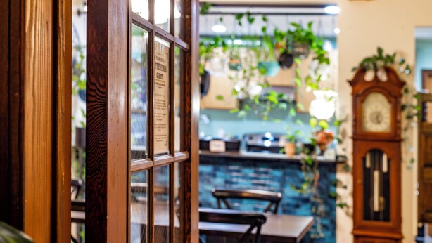 Una ventana con marco de madera que da a una zona de bar, un reloj y plantas colgantes.