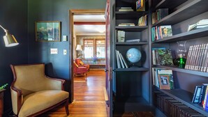Una habitación con piso de madera, un sillón rojo, una estantería llena de libros y un globo terráqueo, y un cuadro en la pared.