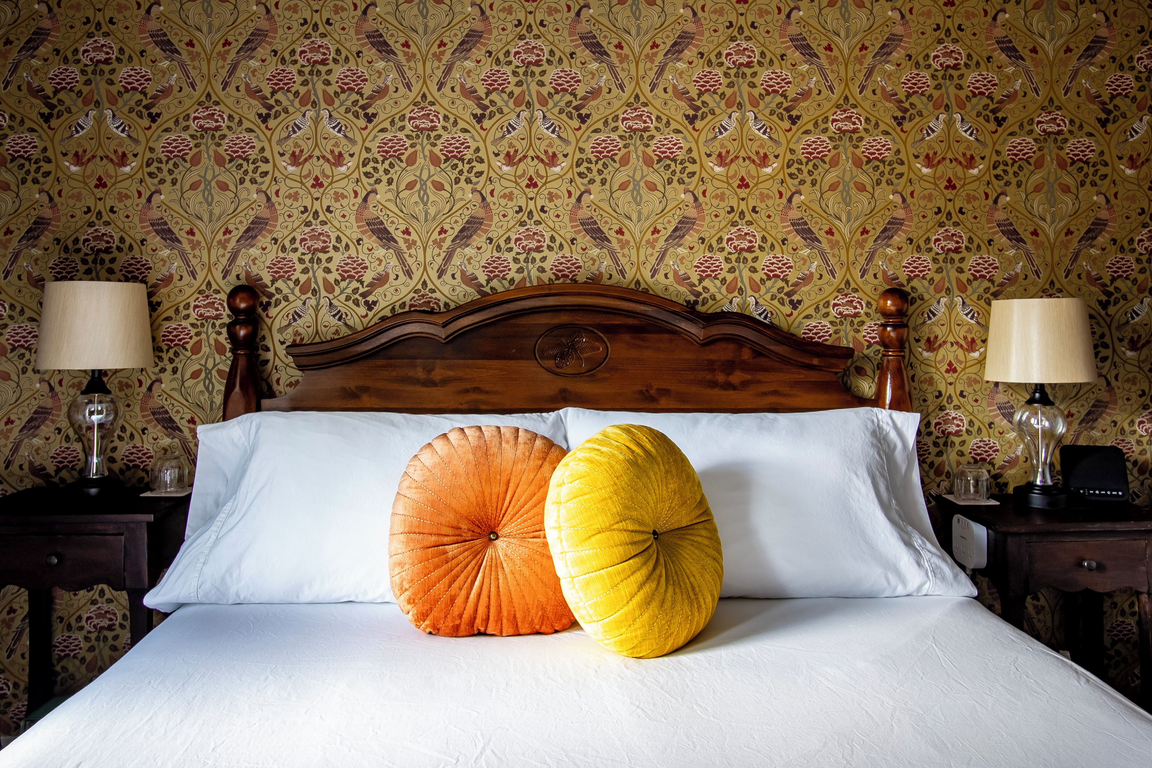 A bed with two large decorative pillows, a wooden headboard, and a patterned wallpaper.