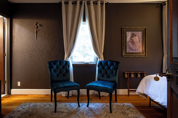 A room with two blue upholstered chairs, a wooden floor, a patterned rug, a window with curtains, a wall-mounted picture, and a bed with a white cover. - #7 Tatoosh Ridge Trail Private Bath -Adults Only (Packwood)