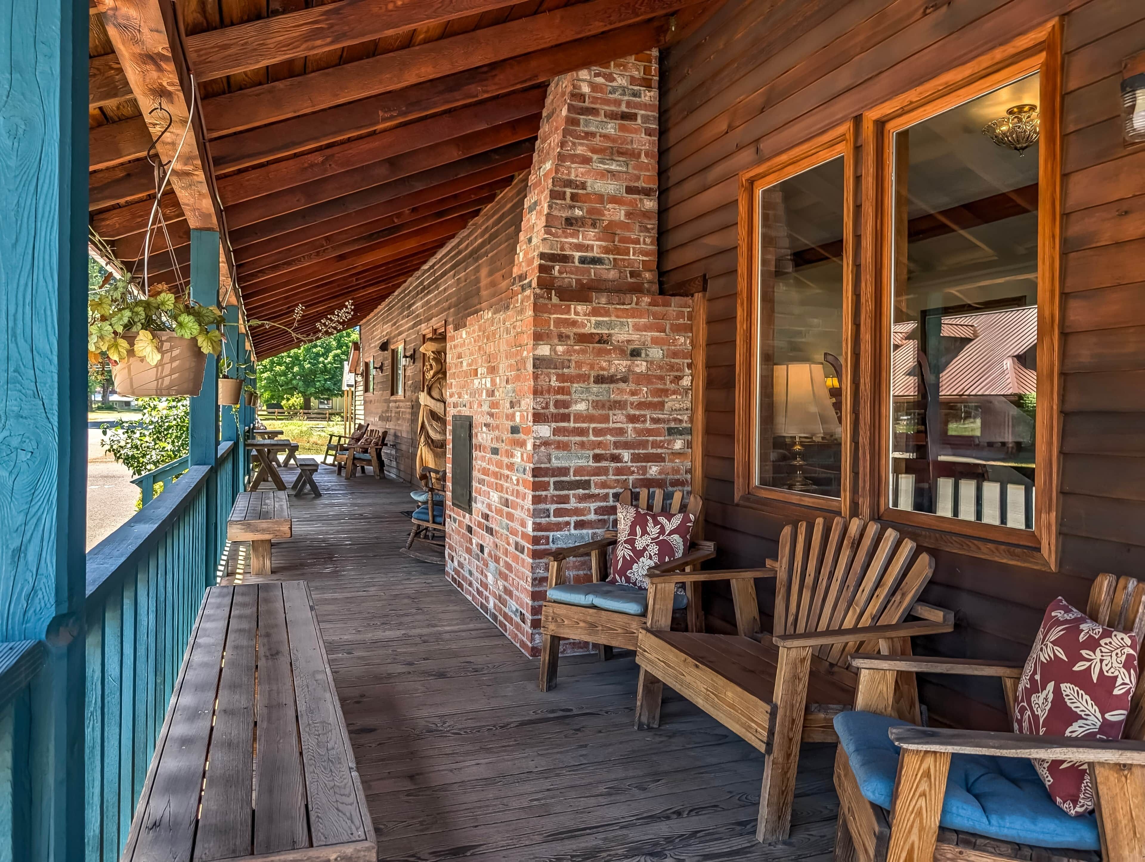 A covered porch with wooden furniture and a brick fireplace.