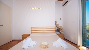 A bedroom with a large bed, wooden headboard, two bedside tables, a wall-mounted light fixture, and a view through a glass door. - Il Greco   (Zakynthos)