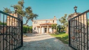A stone house with a tiled roof, a stone pathway leading to the entrance, and a metal gate with a lamp post on top. - Il Greco   (Zakynthos)