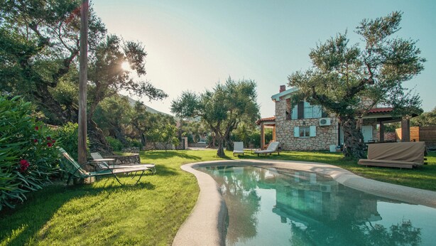 A pool area with a stone house, lounge chairs, and a clear sky. - Il Greco   (Zakynthos)