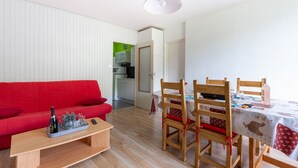 A living room with a red sofa, a wooden coffee table, and a dining area with a table set for two. - L'Ourson des Myrtilles (La Bresse)