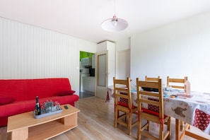 Uma sala de estar com um sofá vermelho, uma mesa de centro de madeira e uma área de jantar com mesa posta para dois.