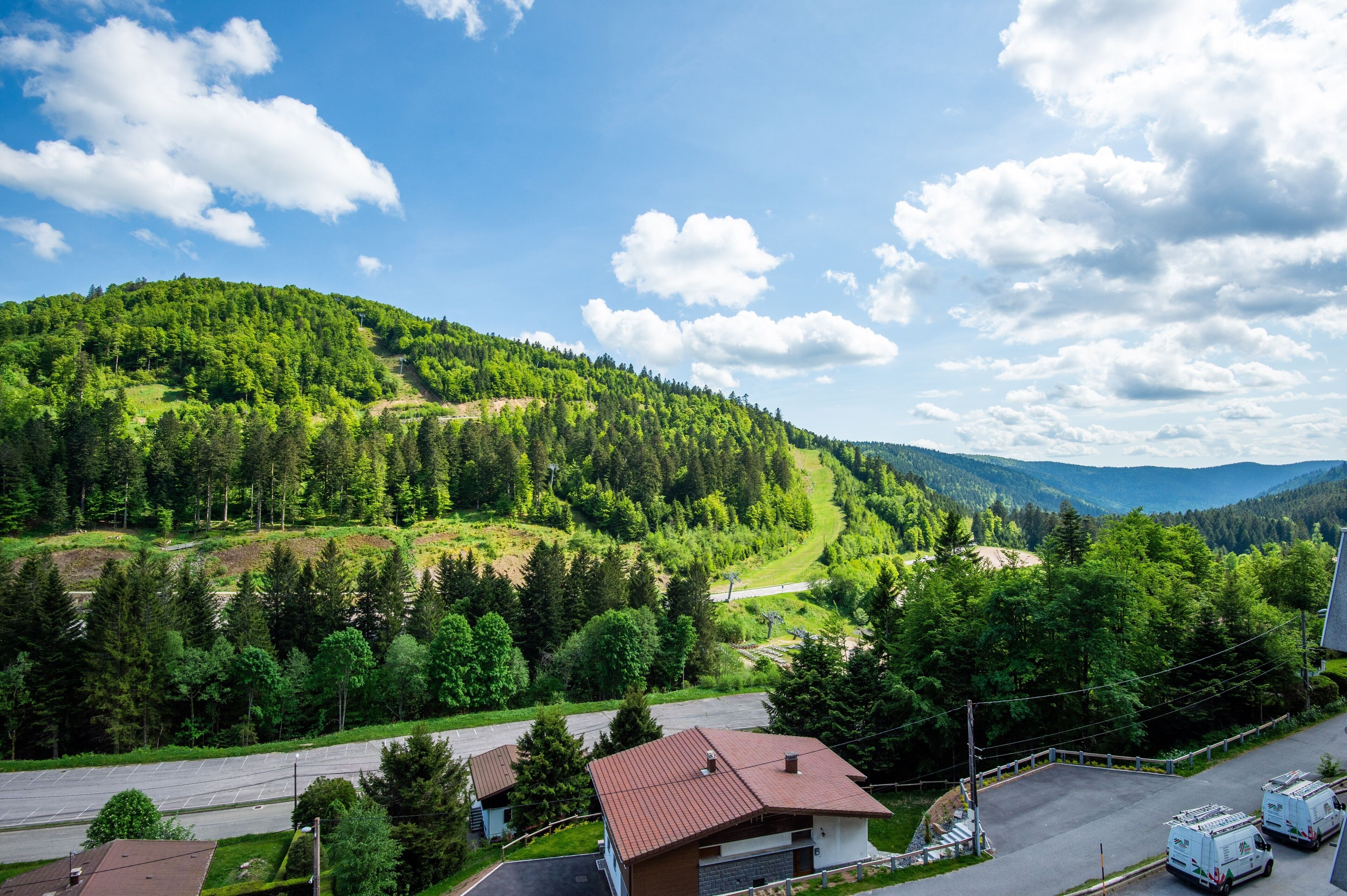 Un paysage rural avec une route, un bâtiment doté d’un toit rouge et une colline boisée.