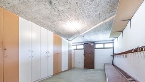 A room with a concrete ceiling, white and brown lockers, a wooden door, and a long bench along the wall. - L'Ourson des Myrtilles (La Bresse)
