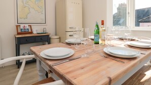 A dining area with a wooden table set for six, a vintage refrigerator, a map on the wall, and a window with a view of buildings.