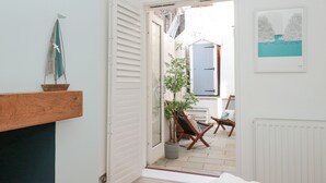 A narrow hallway leading to a balcony with a potted plant and two wooden chairs.