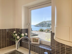 A bathroom with a sink, a window with a view of a coastal town, and a vase with white flowers. - Avondale (Dartmouth)