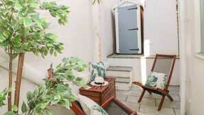 A small, enclosed outdoor space with a wooden chair and a wooden table, a small potted plant, and a door with a window.
