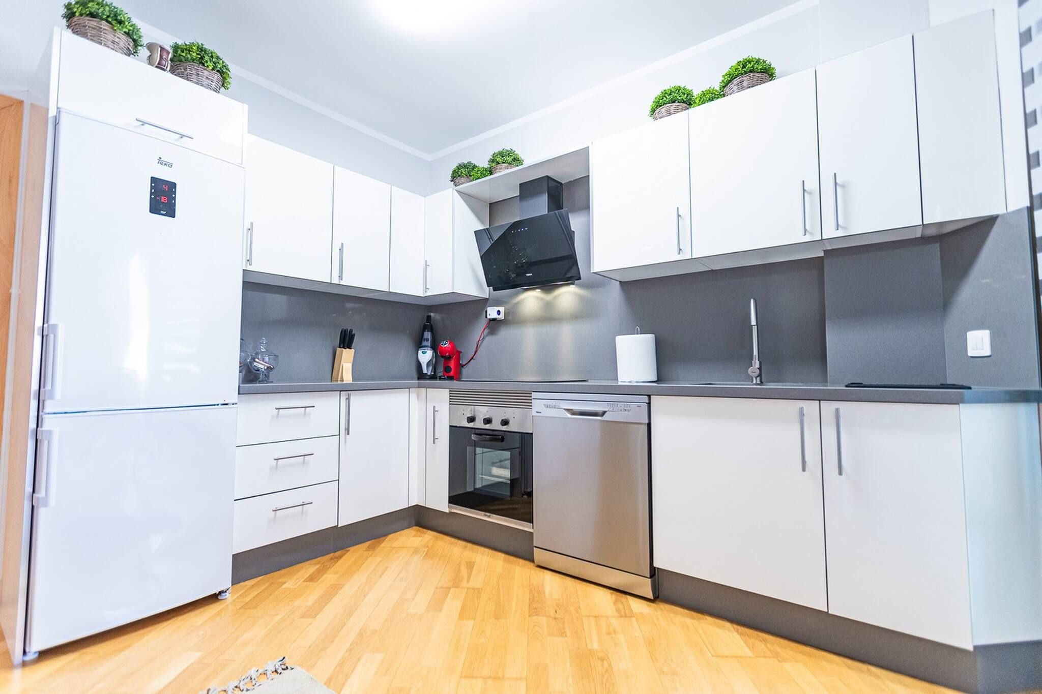 A modern kitchen with white cabinets, a built-in oven, a microwave, and a coffee machine.