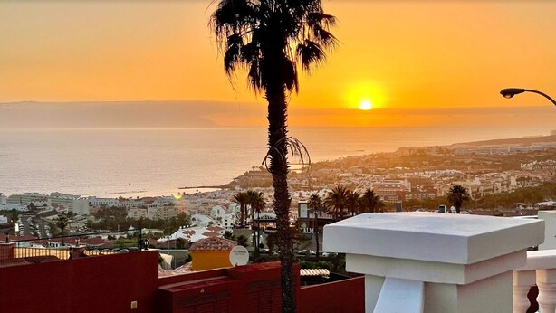 A sunset view over a coastal city with buildings and palm trees. - Amazing Duplex with panoramic ocean views  (Costa Adeje)