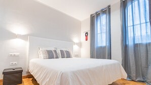 A neatly made bed with white bedding and striped pillows, a bedside table with a lamp, and a window with curtains. - Amazing Duplex with panoramic ocean views  (Costa Adeje)