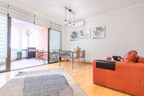 A living room with a red sofa, a dining area with a table and chairs, and a sliding glass door leading to an outdoor patio with a grill.