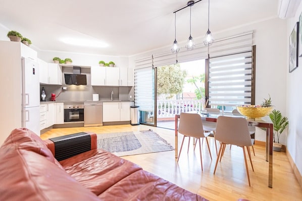 A modern kitchen with white cabinets, a built-in oven, and a dining area with a table and chairs.