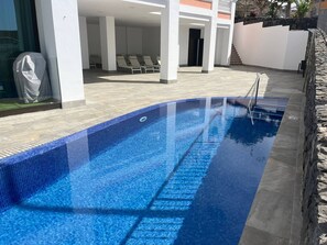 A swimming pool with a tiled edge, surrounded by a covered patio area with lounge chairs.