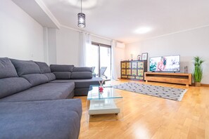 A modern living room with a grey sofa, a glass coffee table, a wooden cabinet with colorful tiles, and a television.