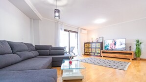 A modern living room with a grey sectional sofa, a glass coffee table, a wooden cabinet with a colorful design, and a television on a wooden stand. - Amazing Duplex with panoramic ocean views  (Costa Adeje)