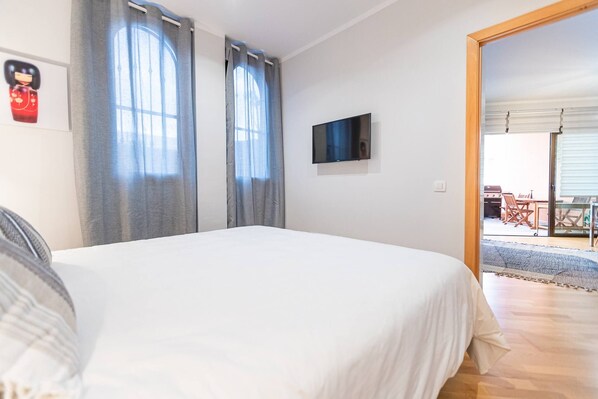 A bedroom with a bed, a flat-screen TV, and a view of an outdoor patio.