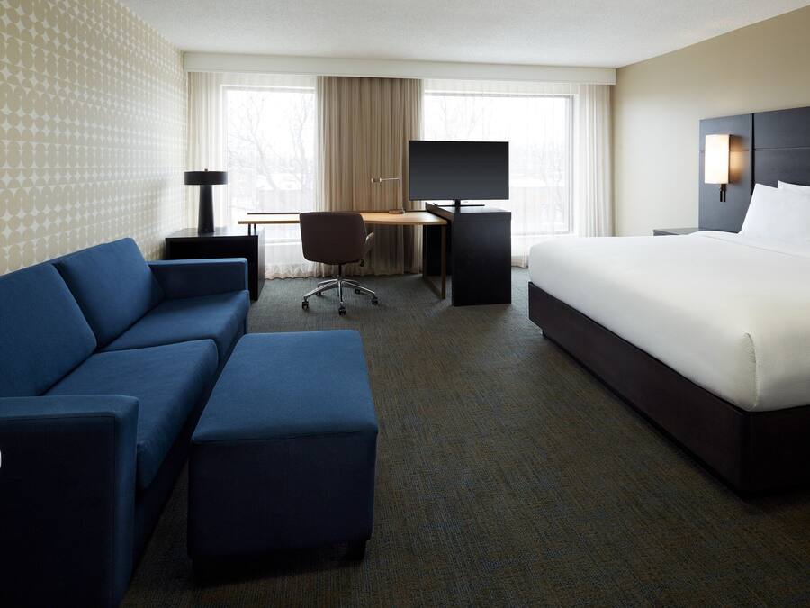 A hotel room with a bed, a desk with a computer, a chair, a sofa, and a small table.