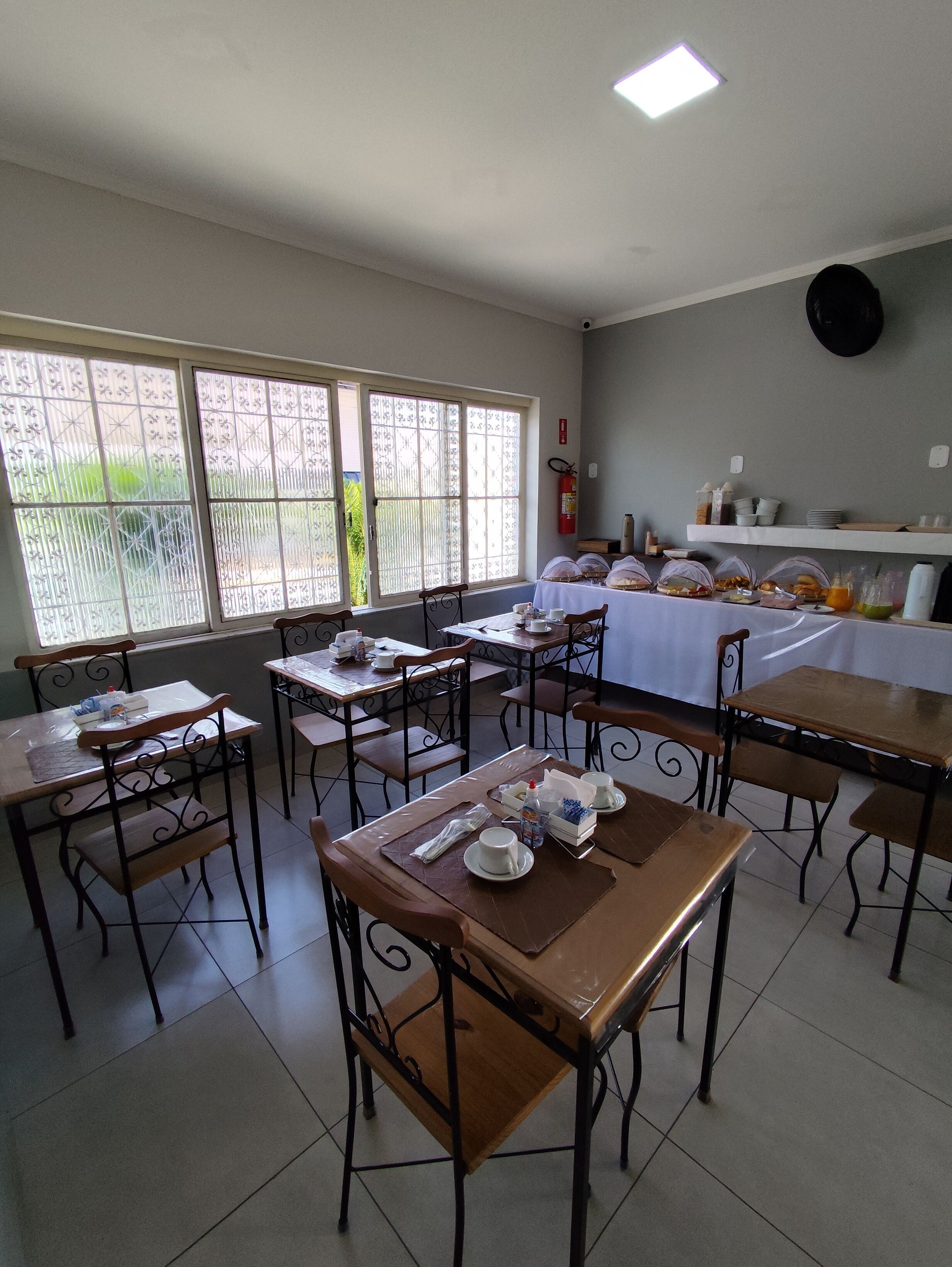 A dining area with tables and chairs, a buffet table with food items, and a fire extinguisher on the wall.